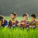 Kids’ Toys Outdoor - four boys laughing and sitting on grass during daytime