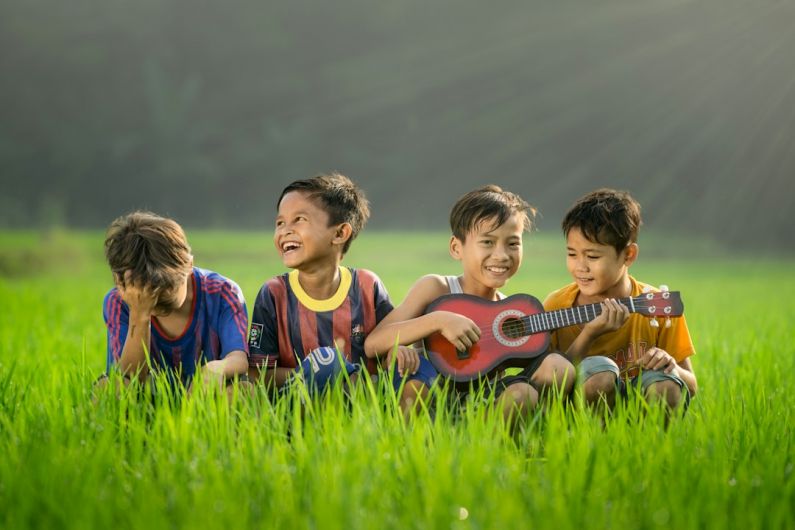 Kids’ Toys Outdoor - four boys laughing and sitting on grass during daytime