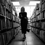 Handbags On Shelf - a woman is walking through a library full of books