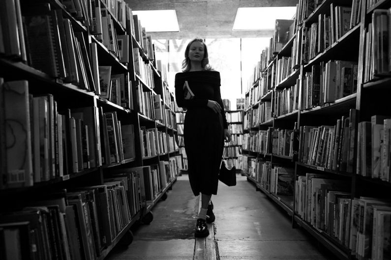 Handbags On Shelf - a woman is walking through a library full of books
