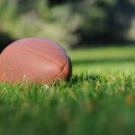 Sports Balls - selective focus photography of brown football on grass at daytime